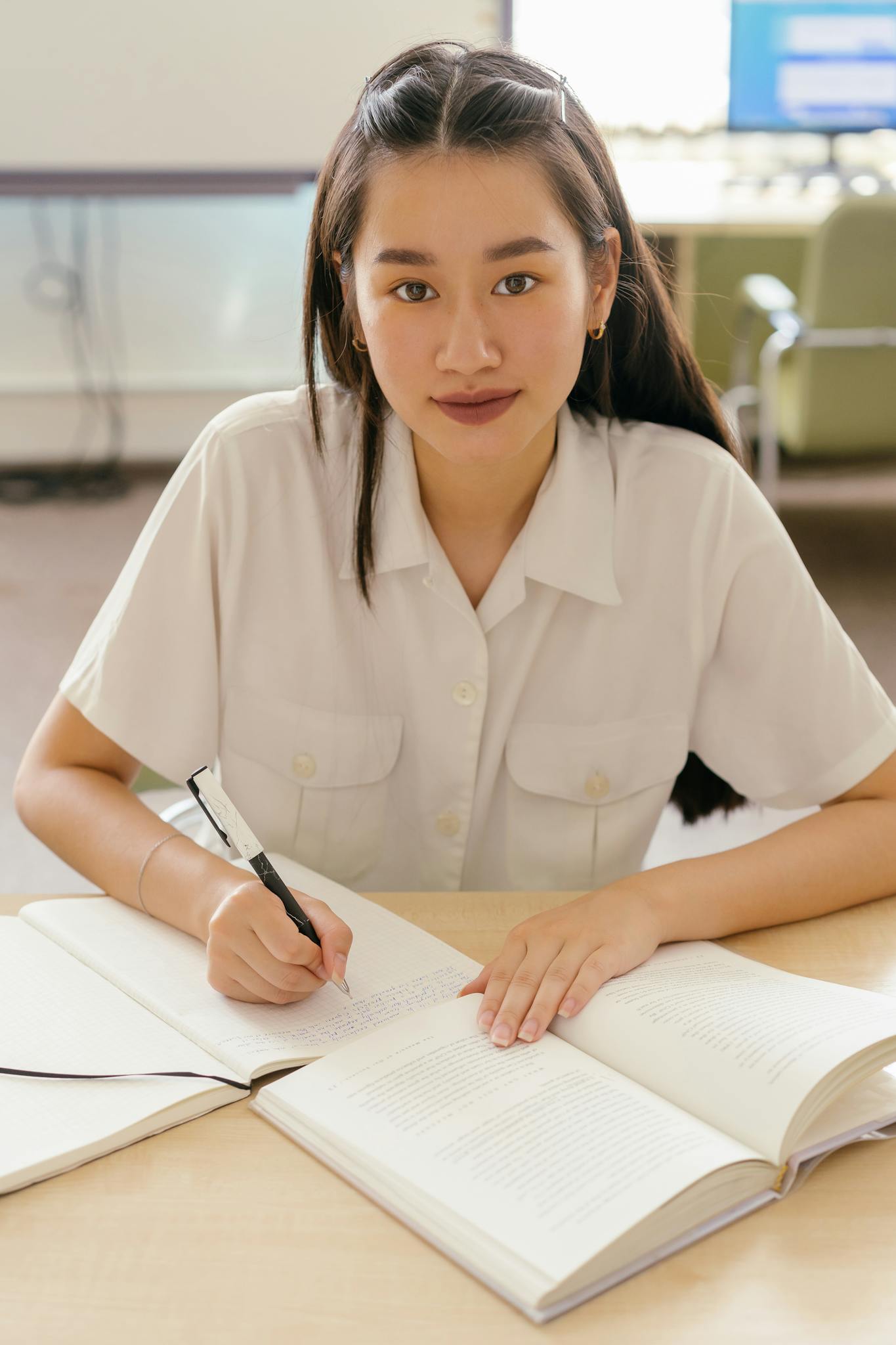 A focused young woman in a library writing in a notebook, symbolizing education and focus.