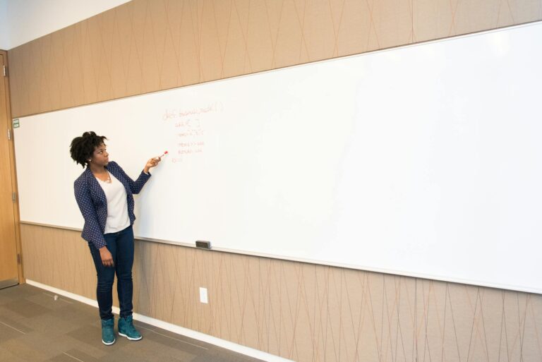 Black female educator explaining concepts on whiteboard in conference room setting.