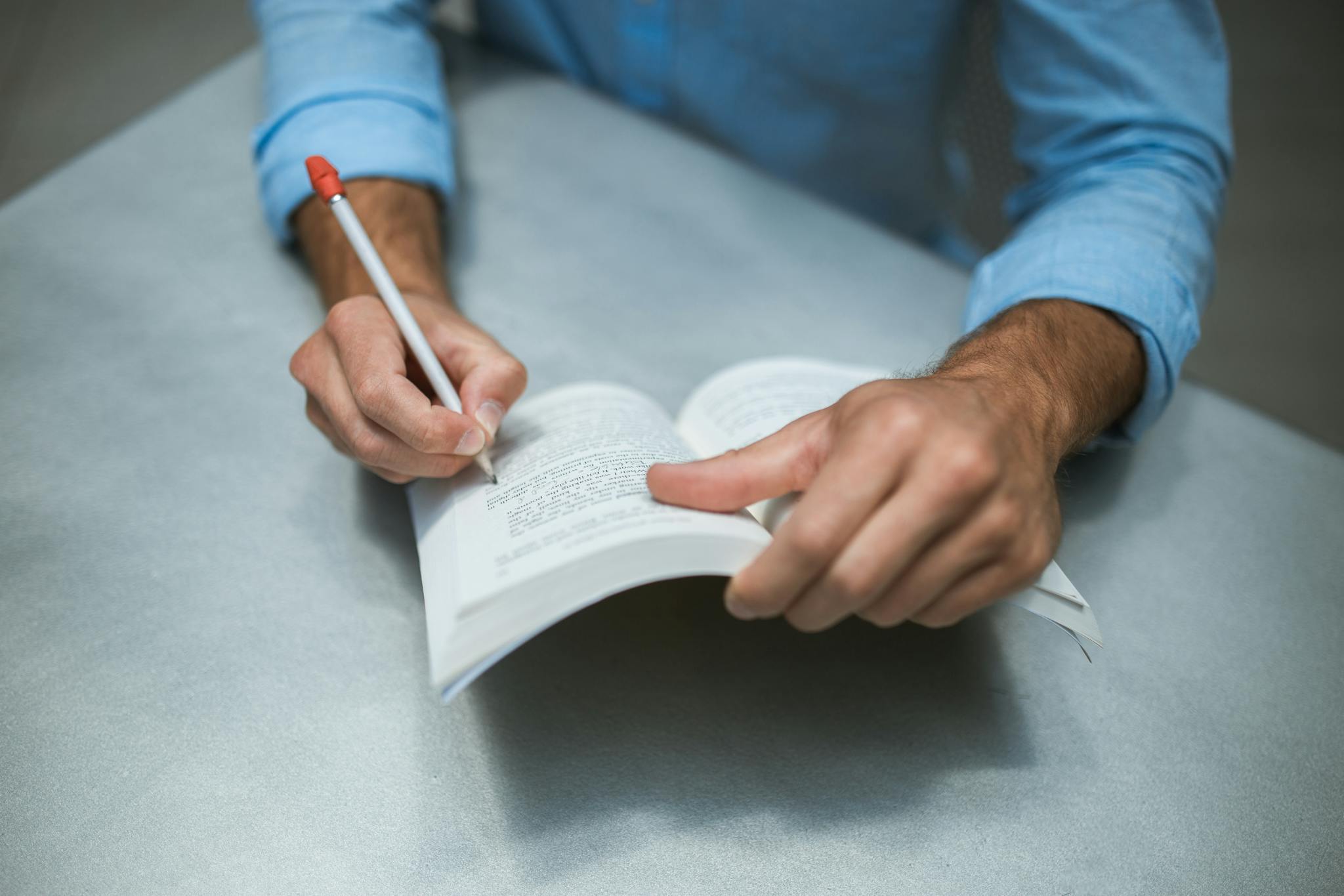 Close-up of a man's hands writing notes in an open book on a desk, symbolizing study and research.